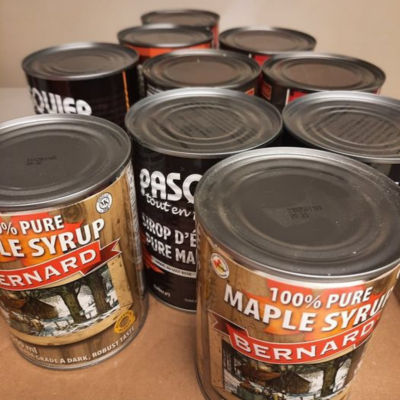Rangée de boîtes de conserve de sirop d'érable pur à 100 % des marques Bernard et Pasco, photographiées de près sur un comptoir, évoquant les produits locaux québécois et l'authenticité des saveurs d'ici.